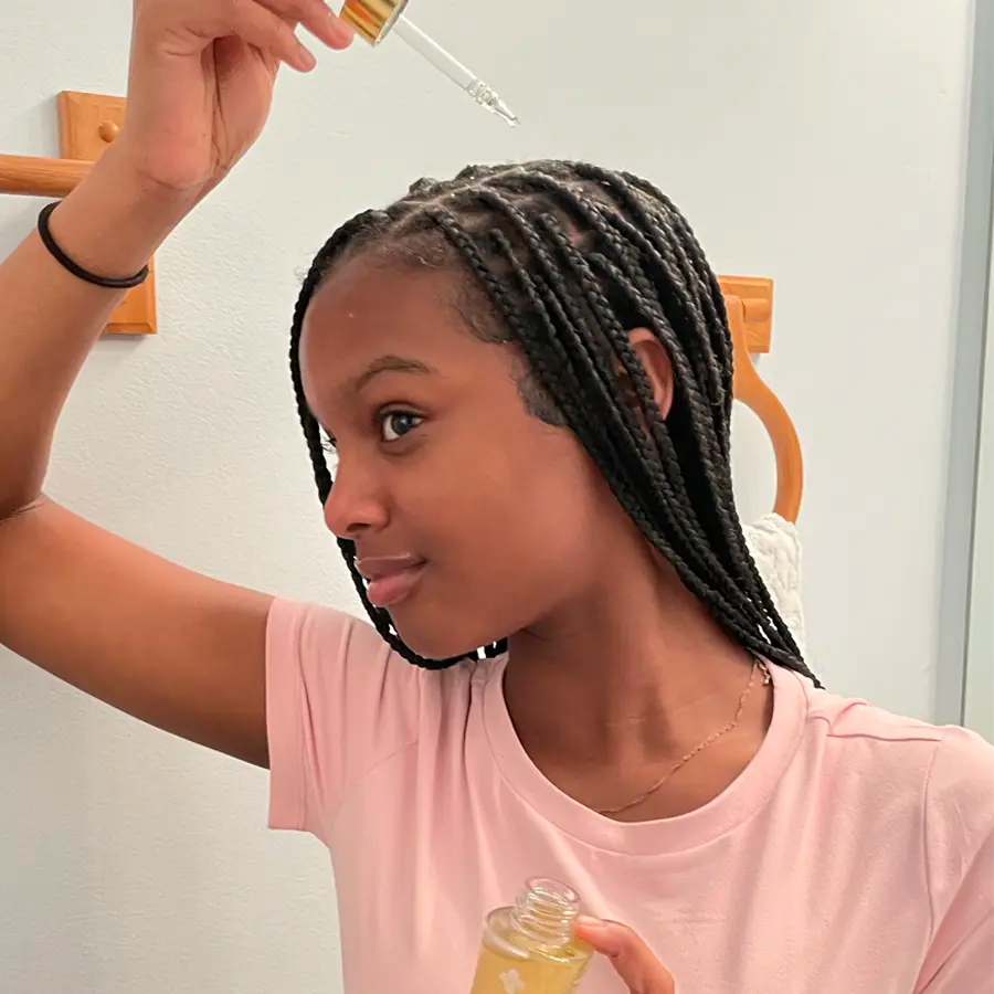 Person applying oil to braided hair using a dropper.